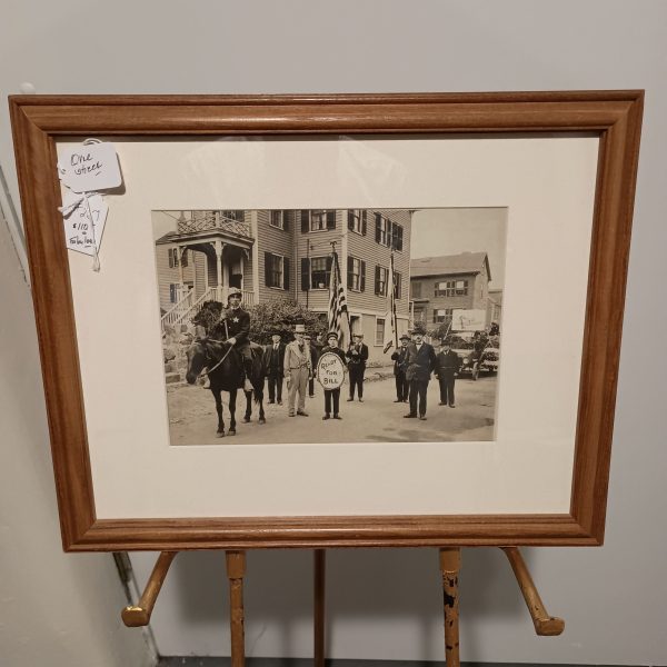 Framed black-and-white vintage photograph of a small-town parade on Orne Street in Marblehead, Massachusetts. The image shows a man on horseback wearing a star badge, several men in early 20th-century attire, an American flag bearer, and a child holding a sign that reads “Ruff for Bill.” The group stands in front of classic New England-style houses, with parked cars visible in the background.